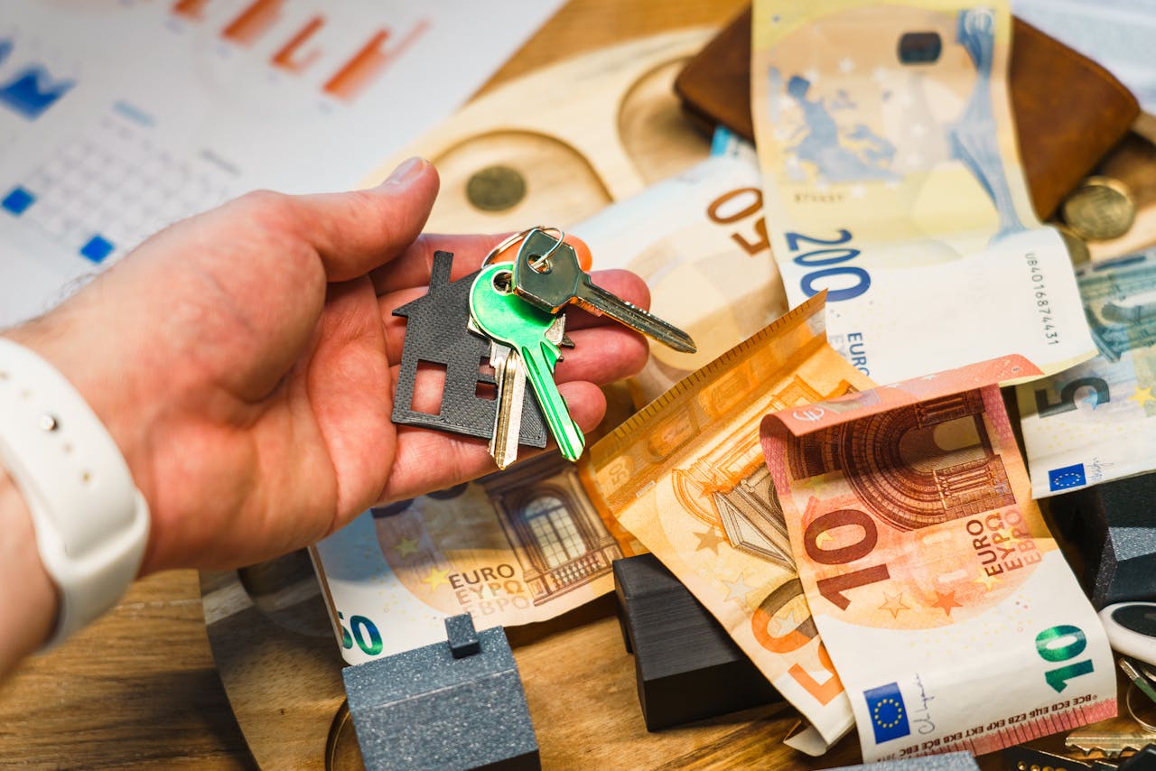 Home A hand holding house keys over euro banknotes, symbolizing real estate and finance.